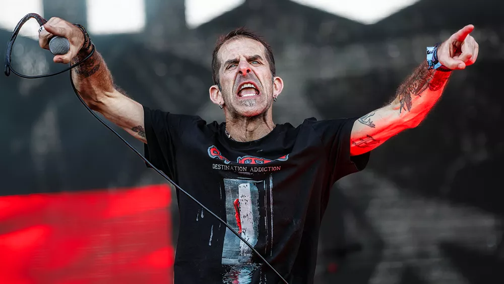 Lamb of God auf der Bühne, Frontmann Randy Blythe im Vordergrund, neues Albumcover mit frischem Logo