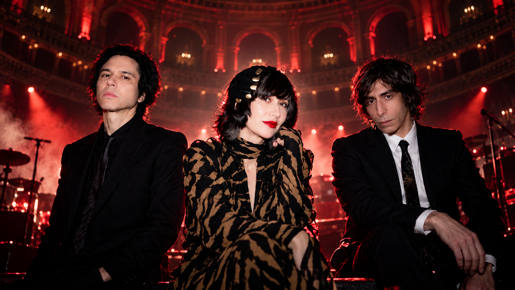 Die Yeah Yeah Yeahs mit Karen O, Nick Zinner und Brian Chase in einer rot beleuchteten Konzertkulisse, angelehnt an einen Auftritt in der Royal Albert Hall.