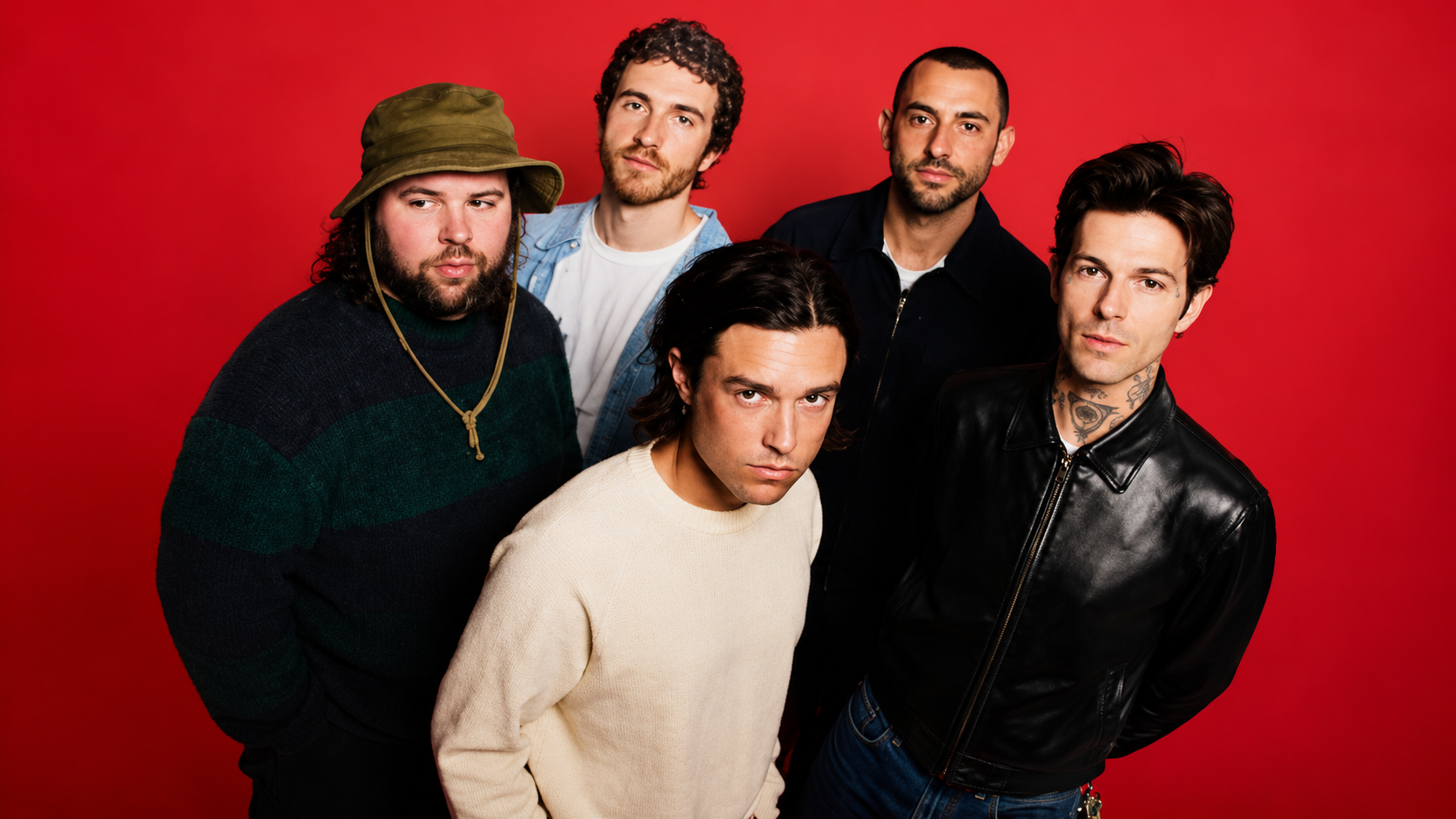 The Neighbourhood posieren zu fünft vor einem kräftig roten Studiohintergrund; die Bandmitglieder tragen lässige Alternative-Rock-Outfits in dunklen und neutralen Farben.